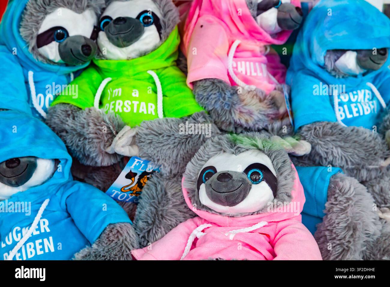 Francfort, Allemagne – 15 mai 2026 : Rangée de peluches paresseux douces portant des sweats à capuche colorés avec des slogans allemands sur un stand de foire à Francfort Banque D'Images