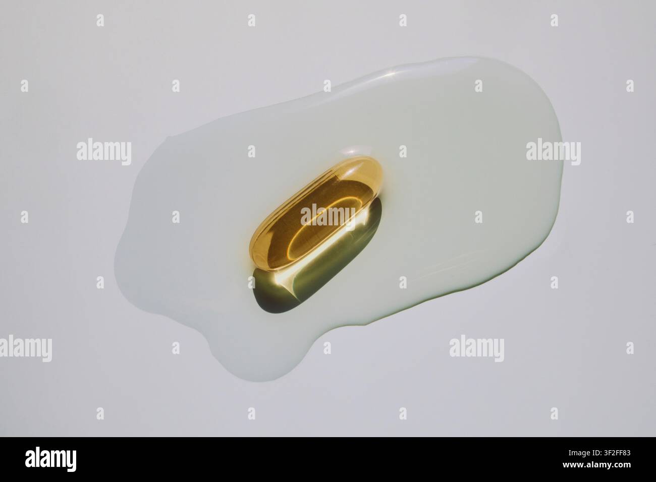 Gélule d'huile de foie de morue dorée flottant dans un liquide huileux clair Banque D'Images
