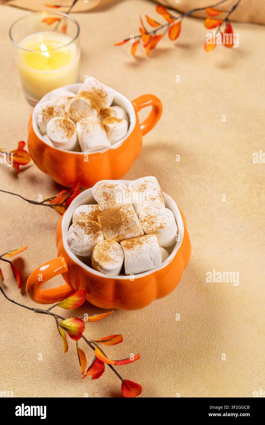 Deux tasses en forme de citrouille remplies de chocolat chaud, garnies de guimauves moelleuses et de cannelle, créant une scène de boisson automnale chaleureuse avec une lumière allumée Banque D'Images