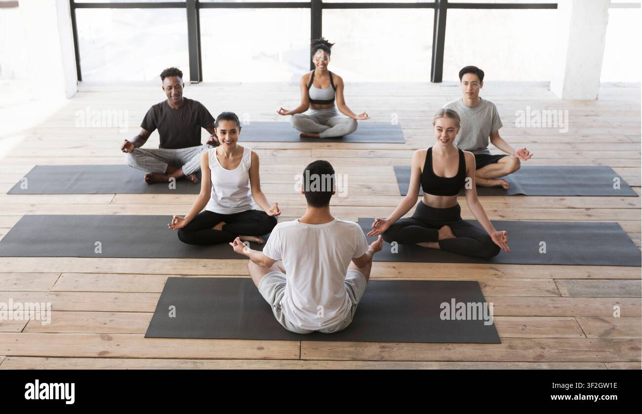 Groupe de jeunes ayant cours de yoga avec entraîneur en studio Banque D'Images