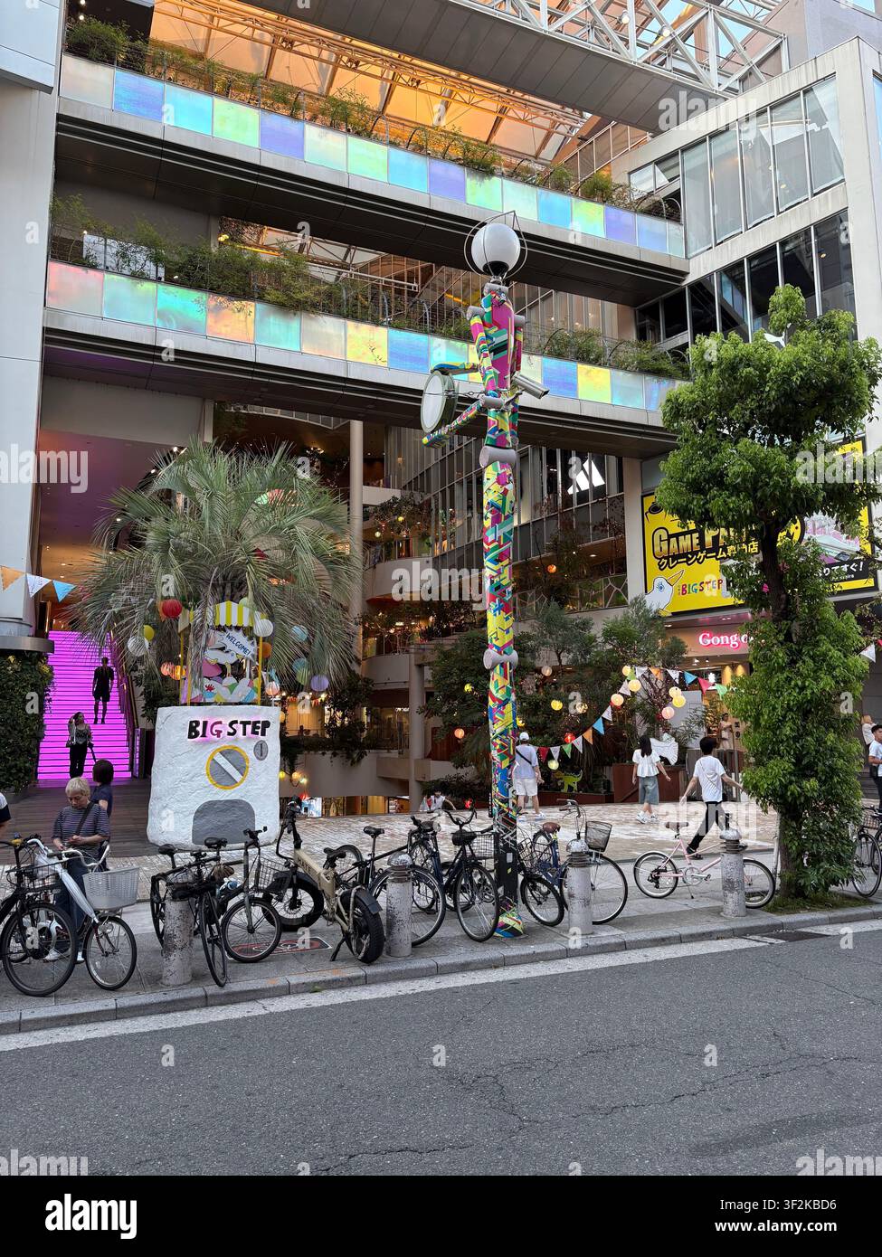 28 juillet 2025, Osaka, Japon – Vue oblique aérienne du centre commercial BIG STEP à Amerikamura avec une façade irisée, une installation sculpturale colorée et des vélos garés. - Image de stock capturée avec un smartphone
