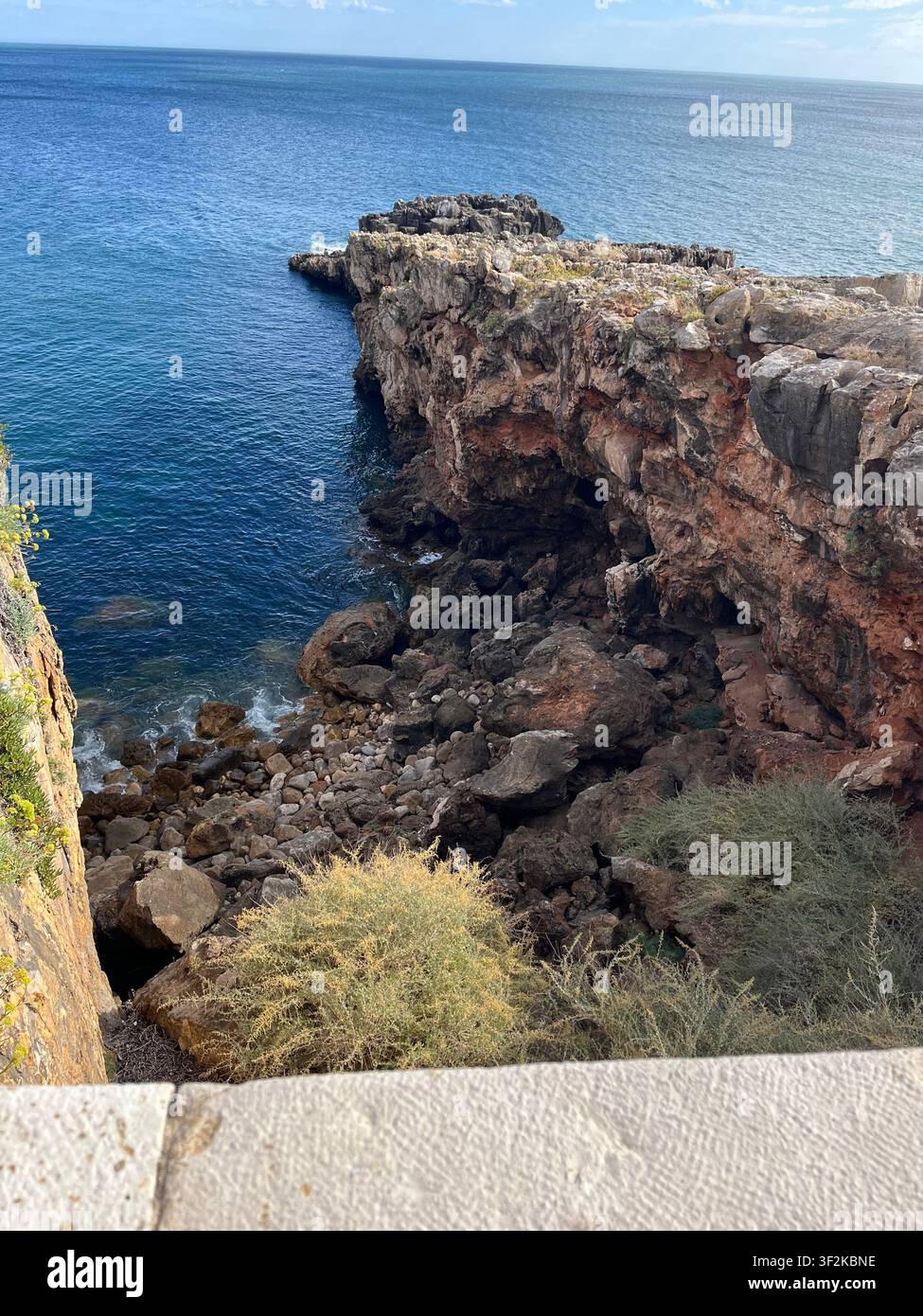 Perspective aérienne depuis un mur de falaise surplombant une côte rocheuse méditerranéenne accidentée avec une mer d'un bleu profond, une grotte et une végétation côtière, Europe. - Image de stock capturée avec un smartphone