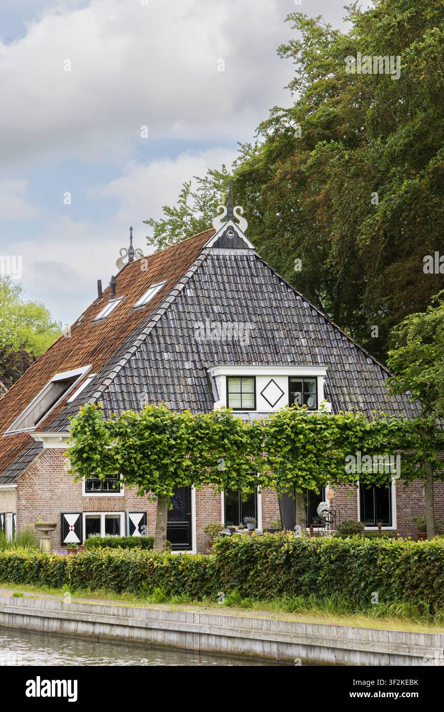 Maison de canal historique charmante à Sloten, Friesland, Pays-Bas présentant une architecture traditionnelle de ferme néerlandaise, un toit de tuiles, des lucarnes et un t Banque D'Images