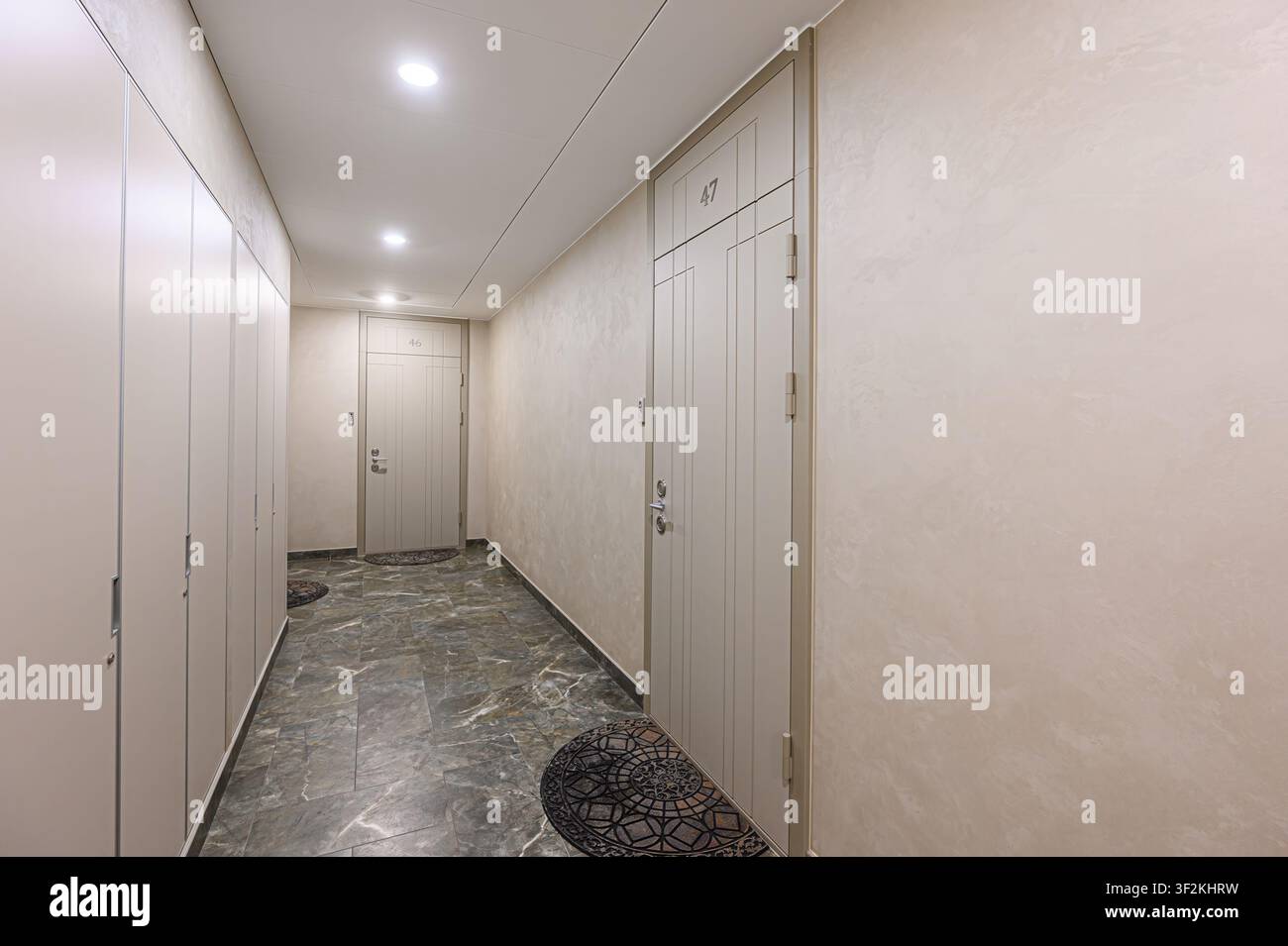 couloir bien éclairé avec des murs de couleur neutre, un sol carrelé et des portes d'appartement portant les numéros 46 et 47. Il y a une rangée de casiers du côté gauche Banque D'Images