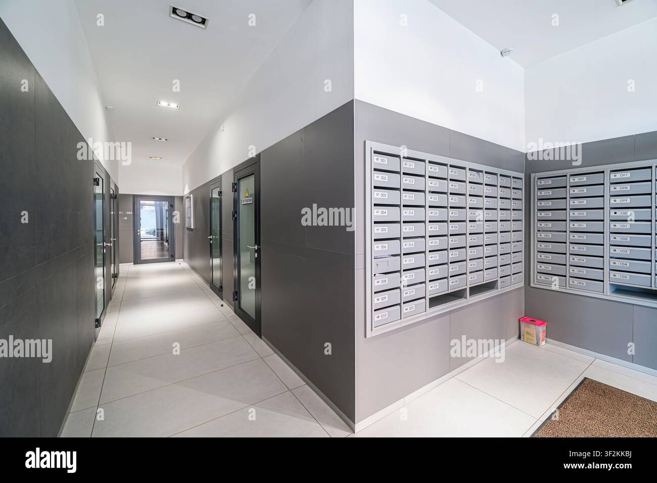 Couloir d'appartement moderne avec boîtes aux lettres et portes de bureau. L'espace est propre avec un schéma de couleurs gris et blanc Banque D'Images
