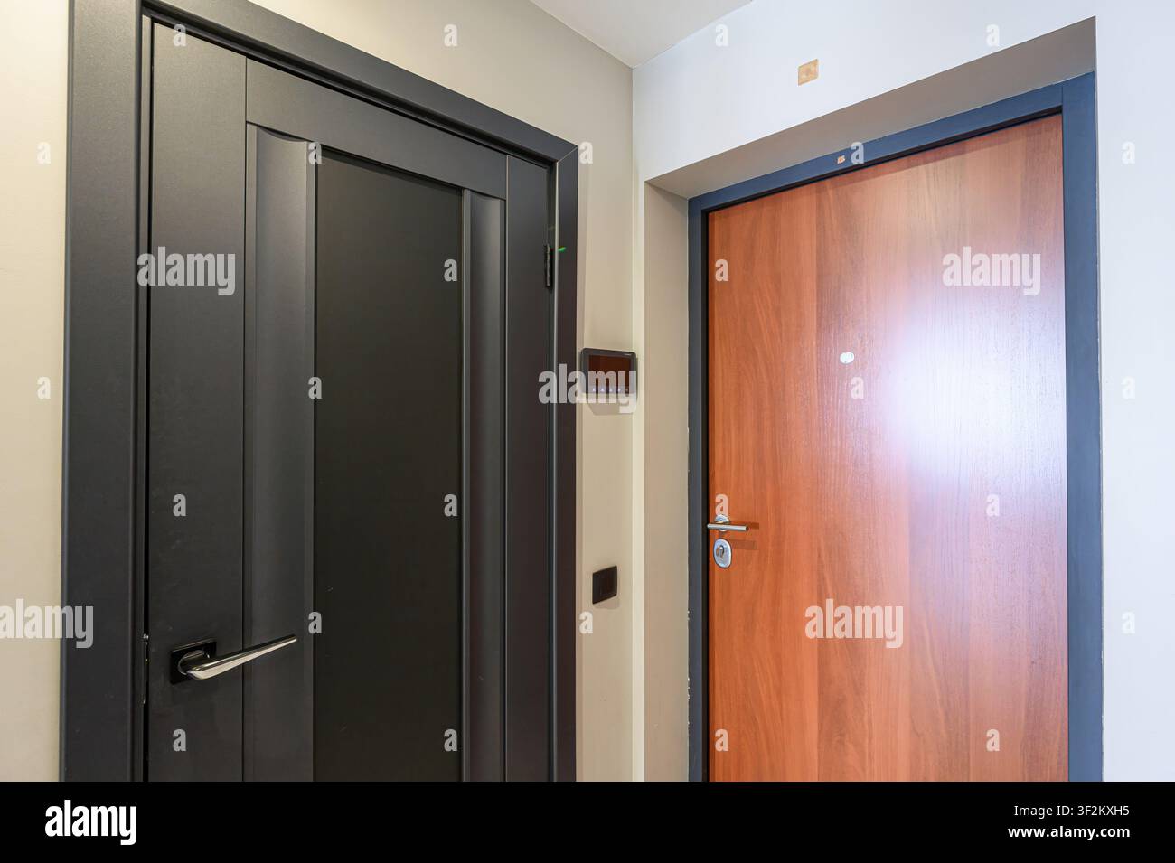 Deux portes, une noire et une boisée, sont encastrées dans un mur de couleur neutre. Un panneau numérique est placé à côté de la porte noire Banque D'Images