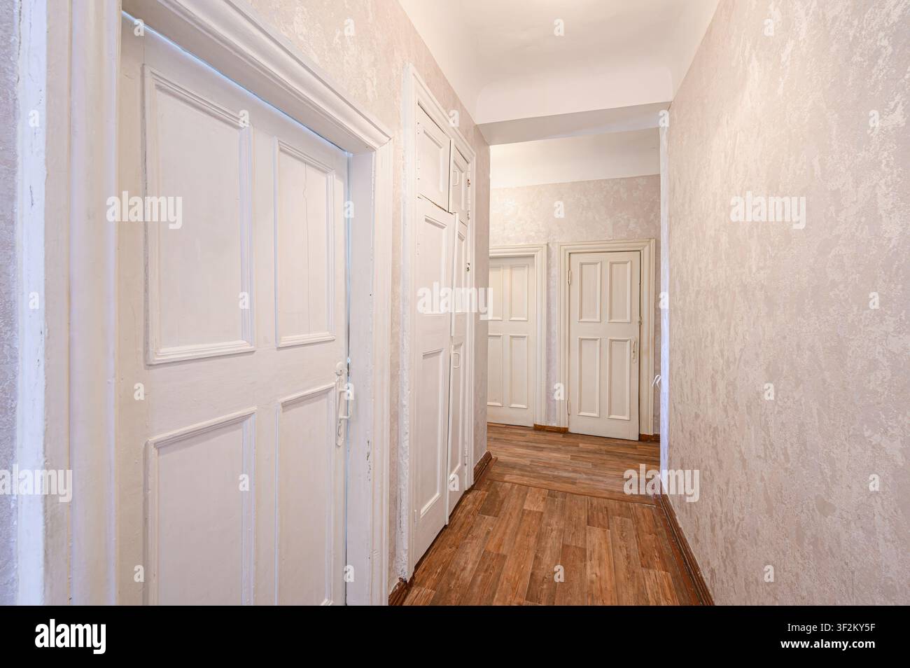 couloir lumineux avec des portes à panneaux blancs et des murs beige clair texturés. Un sol semblable au bois s'étend sur toute sa longueur, menant à d'autres portes au loin Banque D'Images