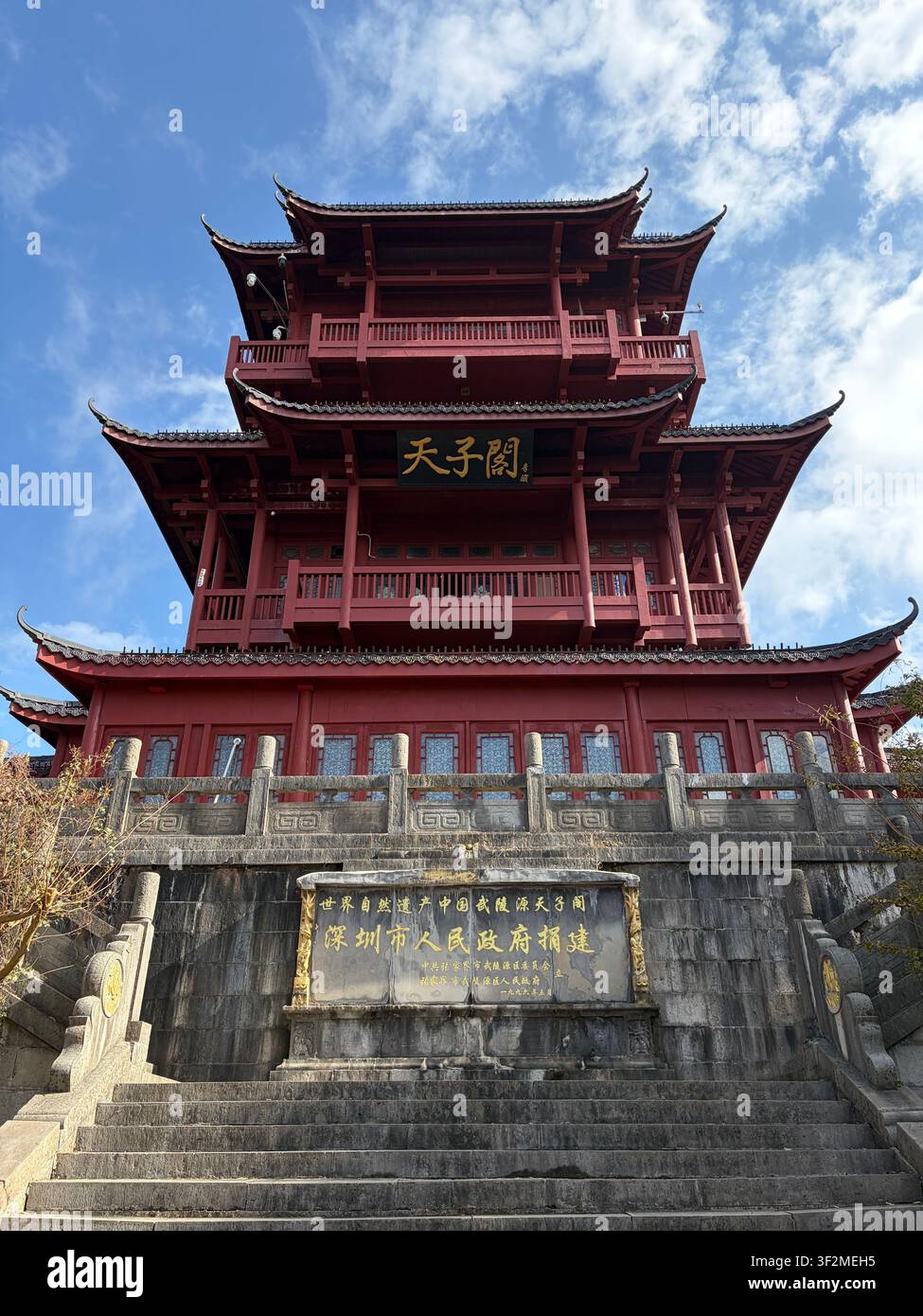 5 novembre 2025, Wulingyuan, Zhangjiajie, Chine – Vue en contre-plongée d’un pavillon chinois traditionnel à plusieurs pans, rouge et orné, avec une calligraphie dorée et un panneau d’inscription en pierre. Banque D'Images