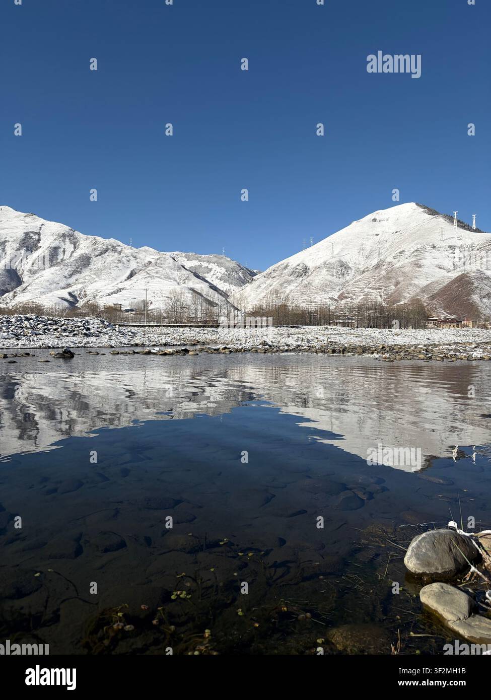 Montagne enneigée se reflétant dans les eaux calmes de la rivière près de Kangding, préfecture de Kardze, Sichuan, Chine, sous un ciel d’hiver bleu et clair. - Image de stock capturée avec un smartphone