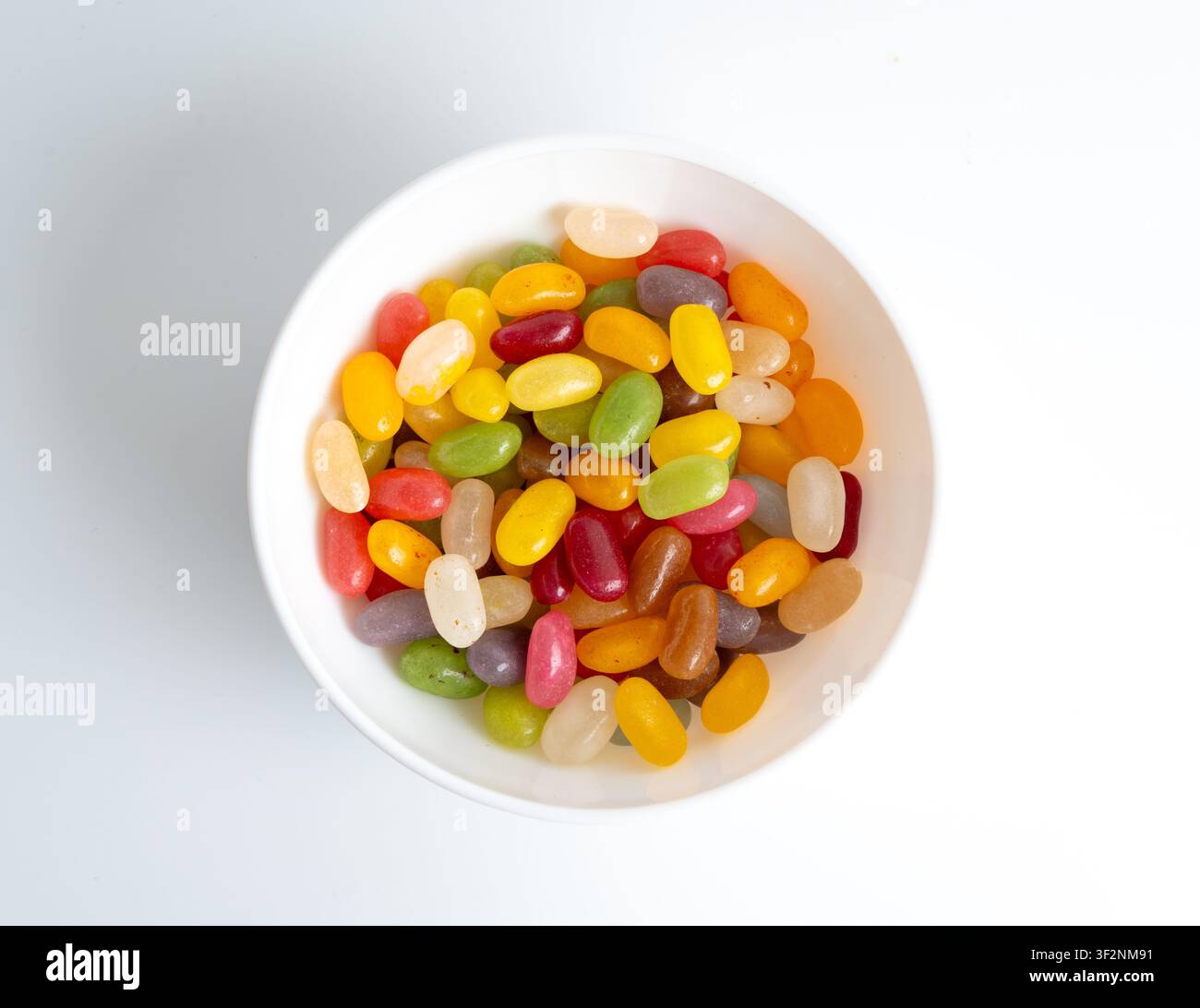 Pile de bonbons gélifiés en forme de haricots dans un bol isolé. Mâcher des pilules de confiture colorées, tas de gouttes de gelée, ensemble de bonbons en gelée sur fond blanc Banque D'Images