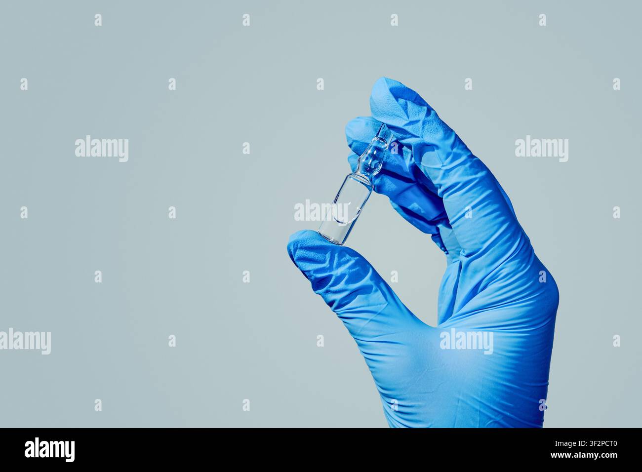 Main gantée tenant une ampoule en verre contenant un médicament liquide sur un fond clair Banque D'Images