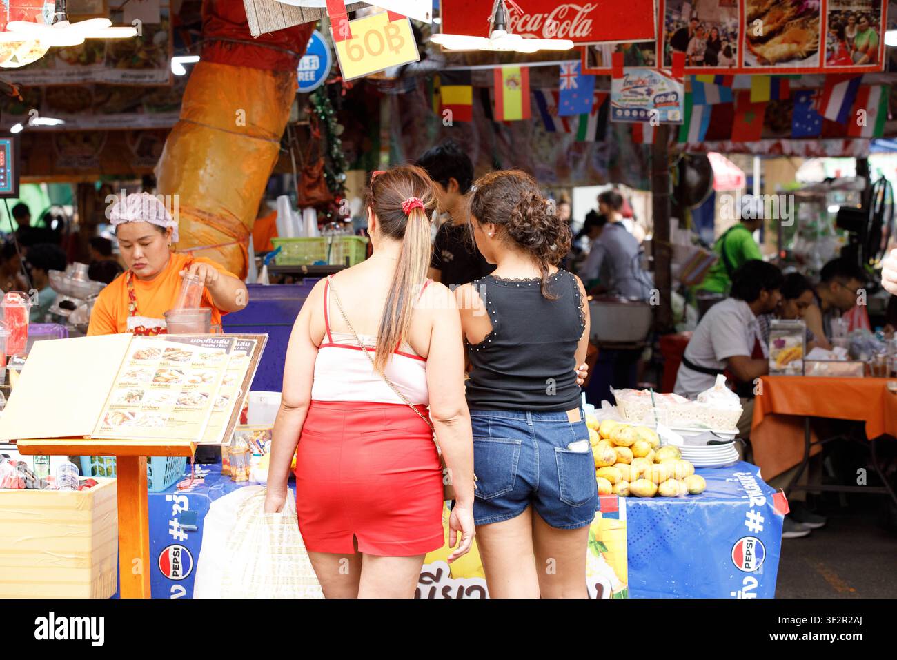 BANGKOK, THAÏLANDE - 12 JUILLET 2026 : Touristes féminines achetant du riz gluant au mango sur un marché en plein air à Bangkok, vue arrière. Banque D'Images