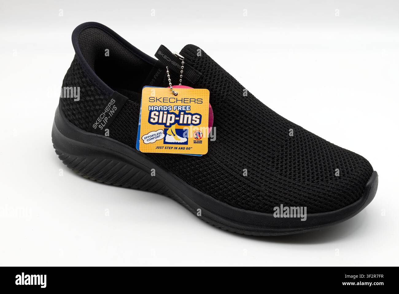 Une paire de baskets Skechers sans lacets noires sur fond blanc avec étiquettes de produit attachées. Banque D'Images