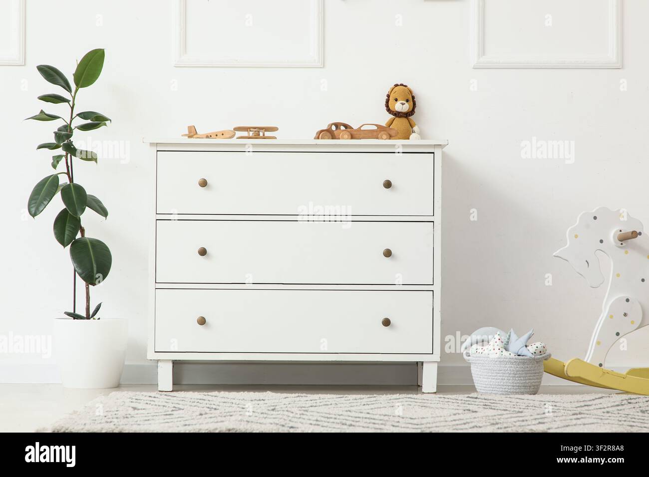 Commode blanche avec des jouets en bois et une plante en pot dans un design d'intérieur minimaliste de chambre d'enfant Banque D'Images
