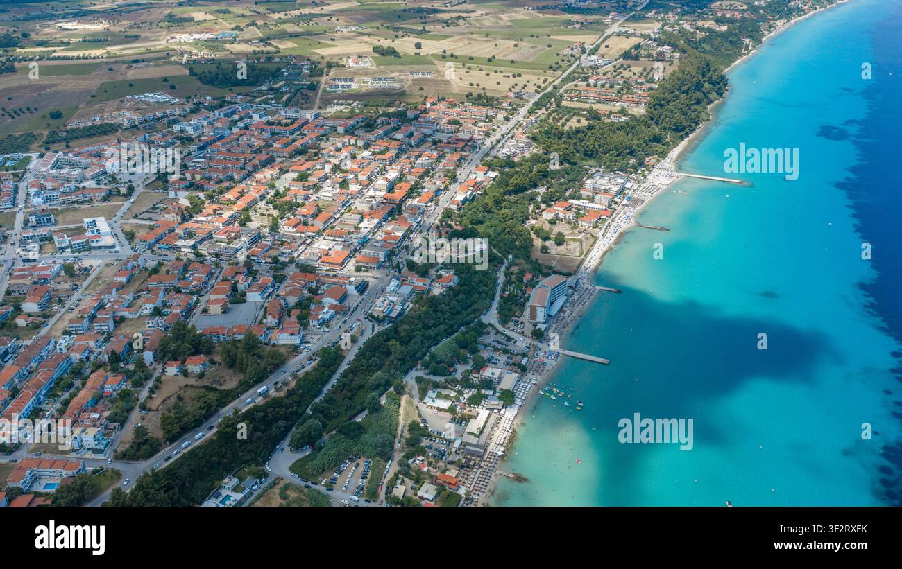 Kallithea, Grèce, 9 juillet 2026. Vue par drone d'une ville côtière densément construite avec des toits en tuiles rouges, une longue plage de sable et une eau turquoise éclatante le long d Banque D'Images