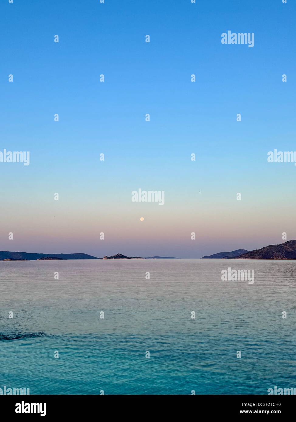 Une mer Adriatique tranquille à l'heure bleue avec la lune se levant au-dessus de l'horizon, entourée de cieux pastel et d'une eau turquoise calme, un paysage minimaliste - Image de stock capturée avec un smartphone