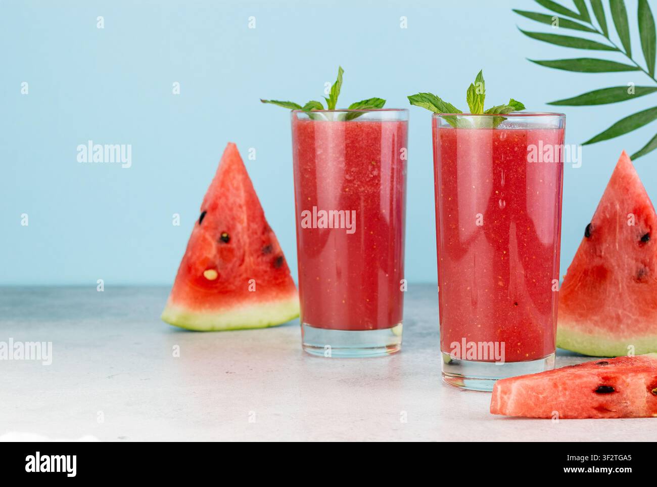 Smoothie à la pastèque frais dans des verres, pastèque tranchée sur fond bleu. Boisson rafraîchissante d'été. Banque D'Images