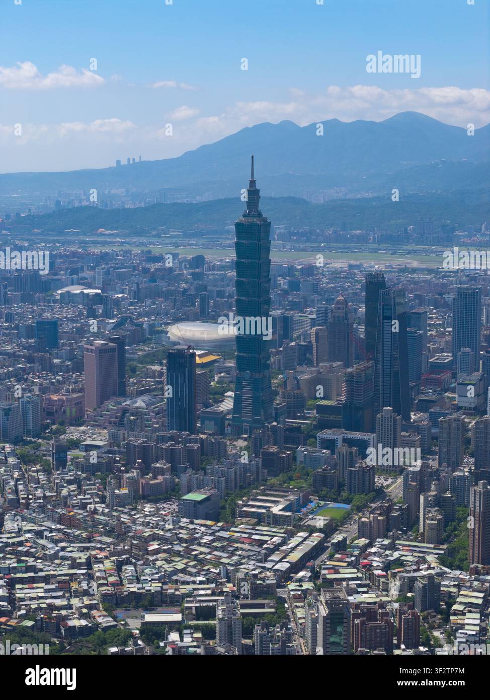 Vue aérienne du gratte-ciel Taipei 101 s'élevant au-dessus du paysage urbain dense, entouré de bâtiments résidentiels, de tours commerciales et d'une montagne lointaine Banque D'Images