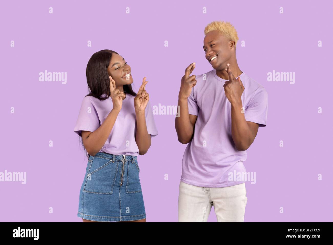 Gai le gars noir et sa petite amie faisant le souhait avec les doigts croisés, mendiant pour la bonne chance sur fond violet Banque D'Images