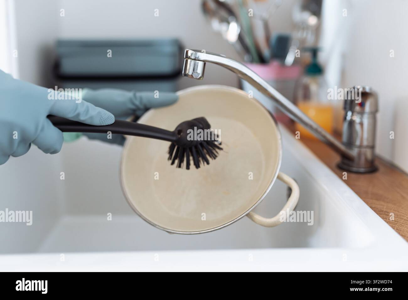 Person mains gantées lavant une poêle à frire avec une brosse Banque D'Images