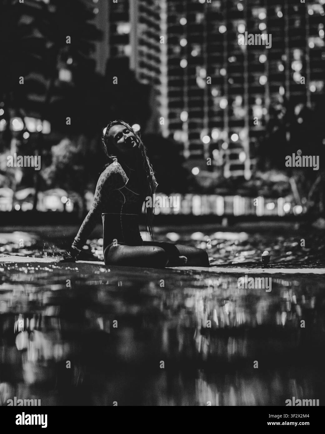 Une femme en maillot de bain est assise sur une planche de surf éclairée la nuit sur l'eau à Waikiki. Banque D'Images