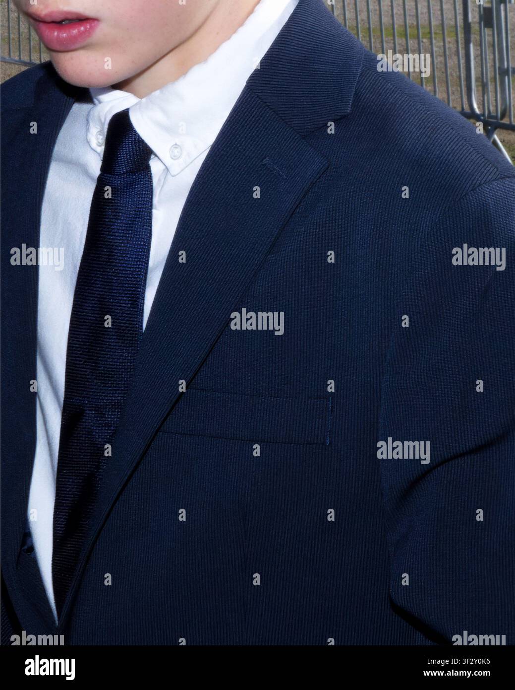 Portrait en gros plan d'un adolescent portant un costume bleu foncé, une chemise blanche et une cravate lors d'un événement formel en plein air Banque D'Images