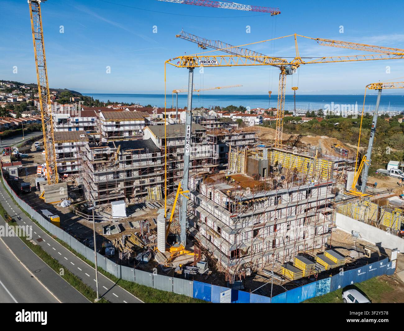 Vue aérienne d'un chantier de construction avec plusieurs grues jaunes, des immeubles d'appartements inachevés et des échafaudages près de la mer Adriatique à Izola Banque D'Images
