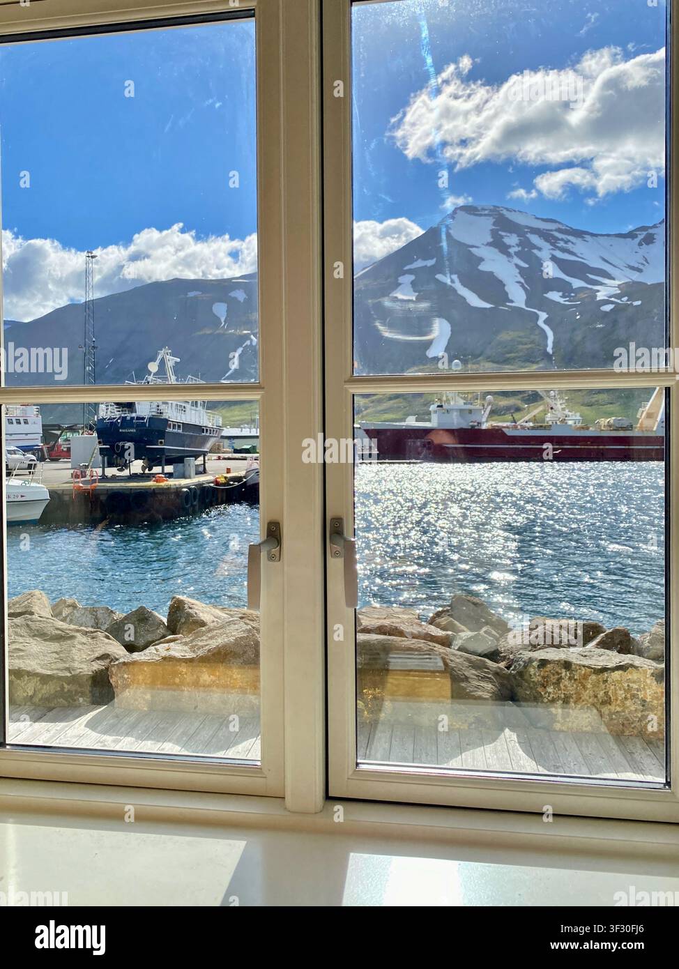 Vue du port de Siglufjörður depuis la fenêtre de l'hôtel, montagnes enneigées, mer, bateaux de pêche sous un ciel bleu clair, Islande du Nord - Image de stock capturée avec un smartphone
