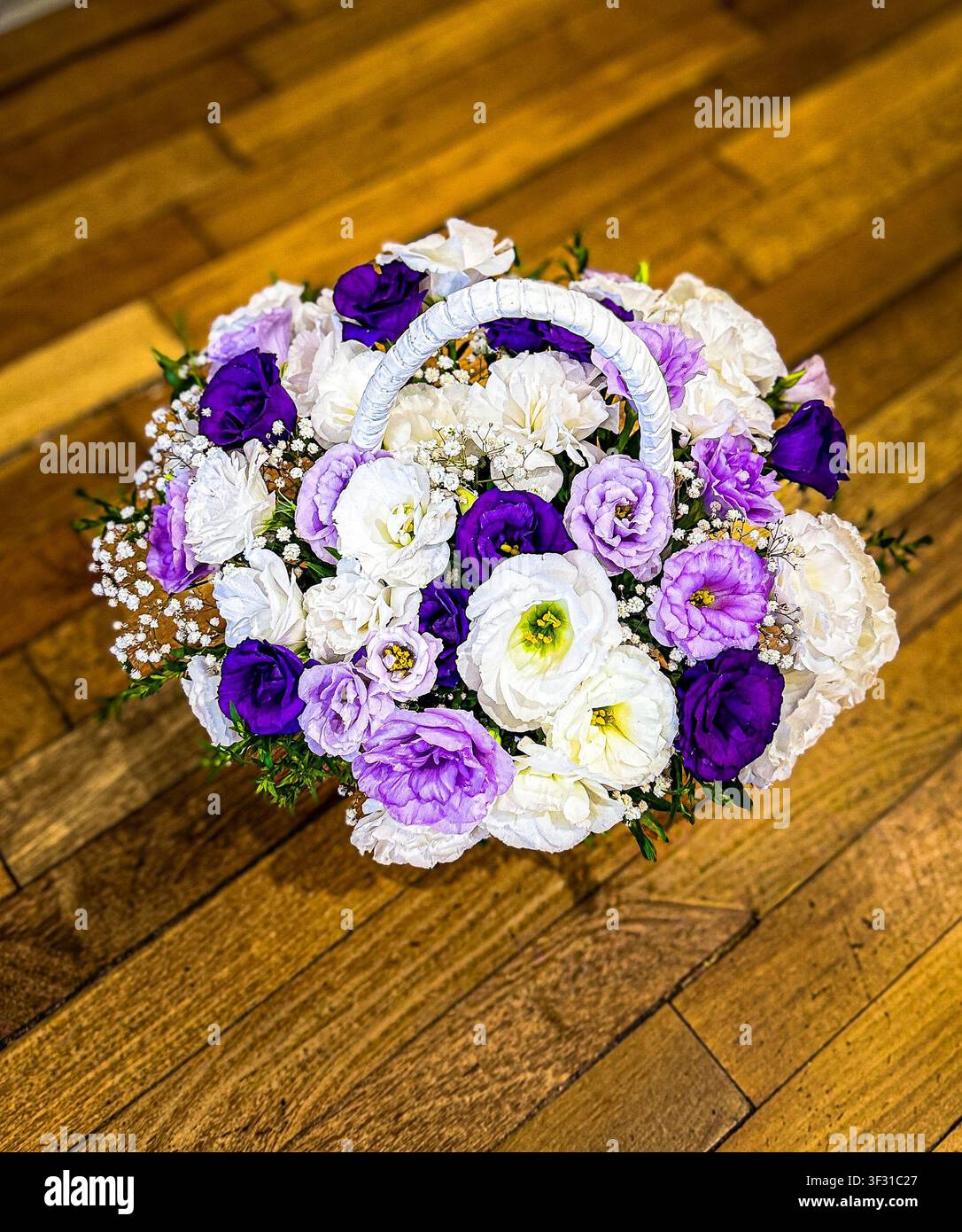 Une vue de dessus d'un magnifique arrangement floral comprenant des fleurs de lisianthus blanches et violettes dans un panier en osier blanc posé sur un sol en bois. Banque D'Images