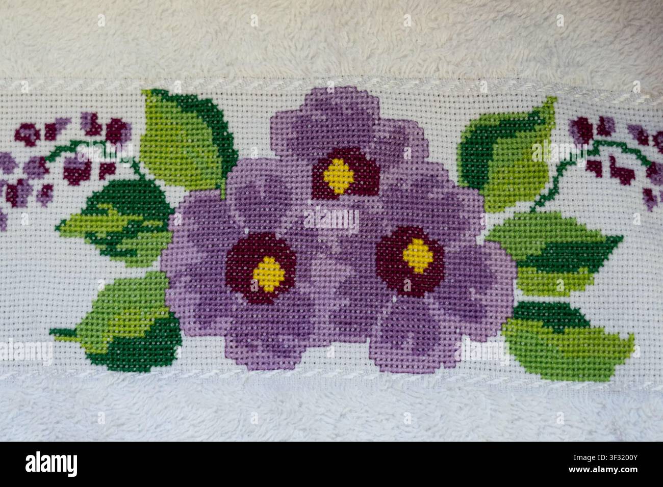 Modèle de point de croix représentant des violettes violettes avec des centres jaunes et des feuilles vertes. Banque D'Images