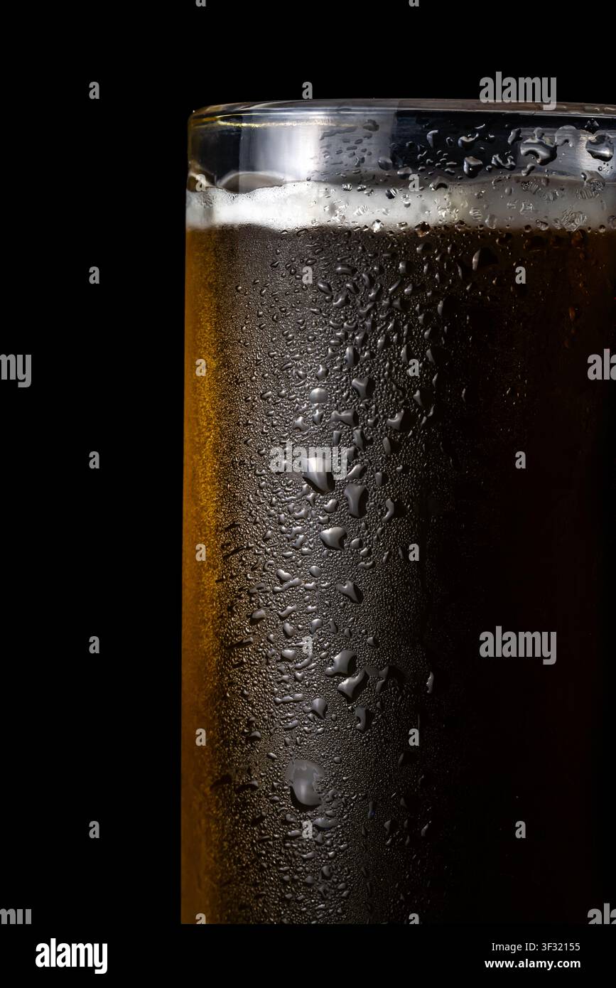 Bière sombre et froide remplit un grand verre parsemé de gouttes d'eau à l'extérieur sur un fond sombre, dans un cadre de bar Banque D'Images