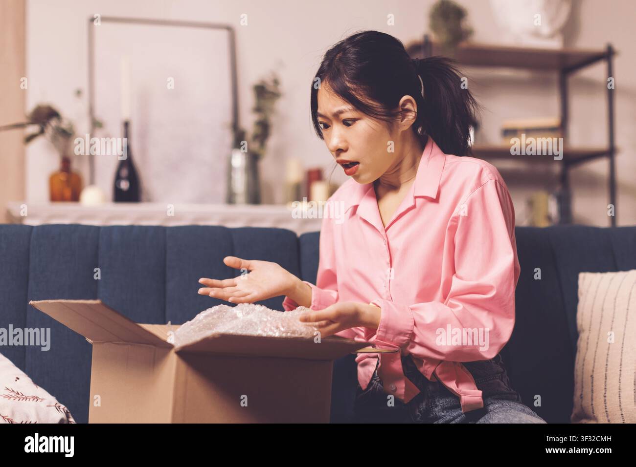 Femme asiatique inquiète ouvrant un paquet avec du papier bulle à la maison, concept de surprise Banque D'Images