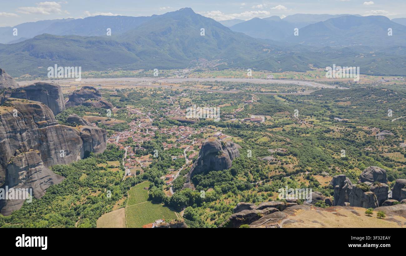 Plan panoramique par drone des piliers rocheux des Météores et du village de Kastraki dans la vallée avec une chaîne de montagnes au loin sous un ciel bleu dans la région de Thessalie en Grèce en su Banque D'Images