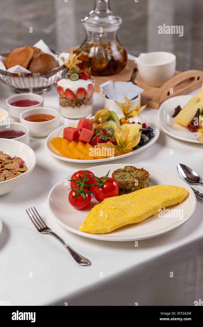 Table de brunch luxueuse avec omelette, tomates, pâtisseries, fruits et thé Banque D'Images