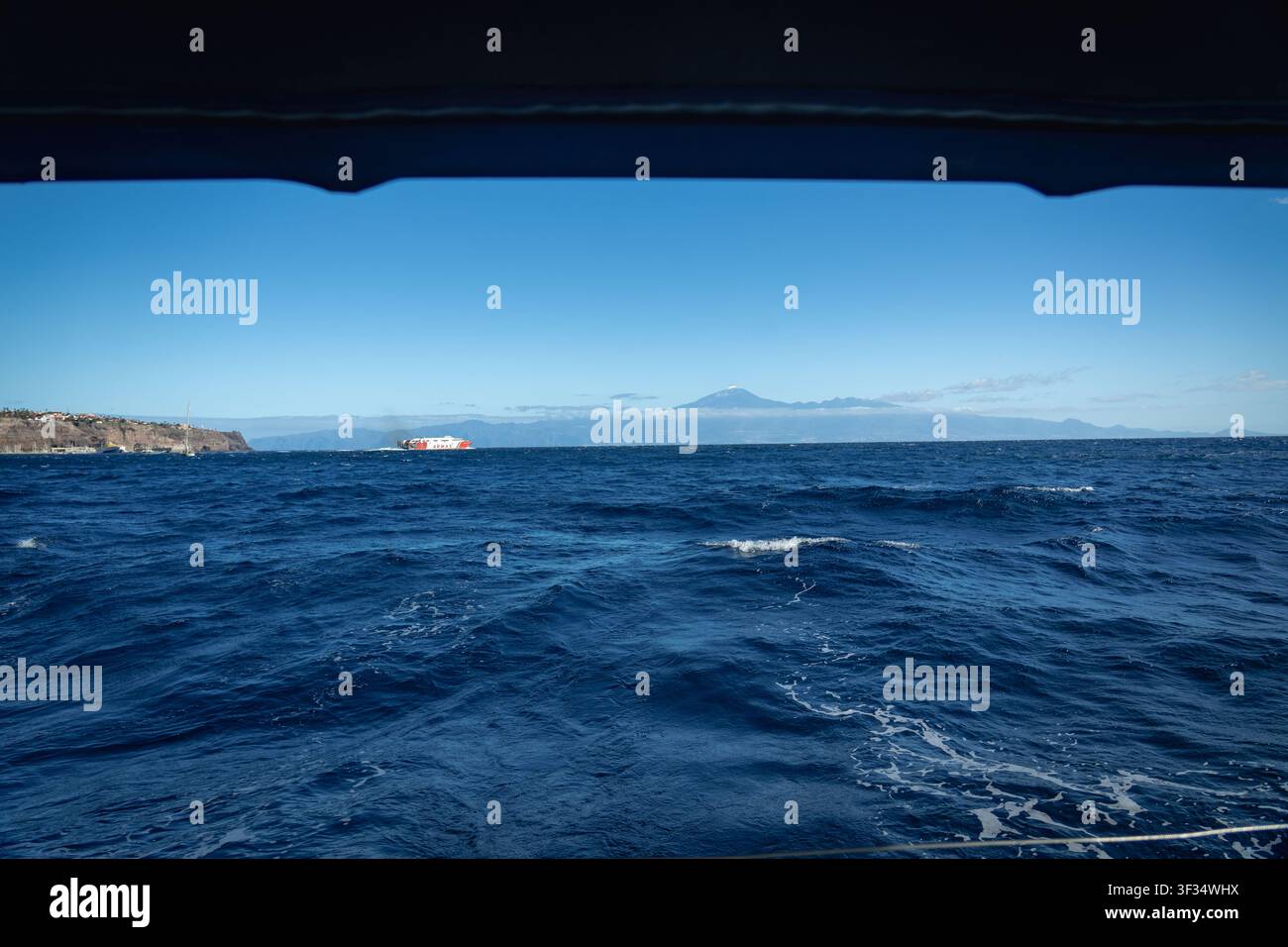 Un ferry rapide traverse le détroit avec le sommet enneigé du Teide à Tenerife à l'horizon, encadré par la toile d'un voilier au large de La Gomera, îles Canaries, Espagne. Banque D'Images