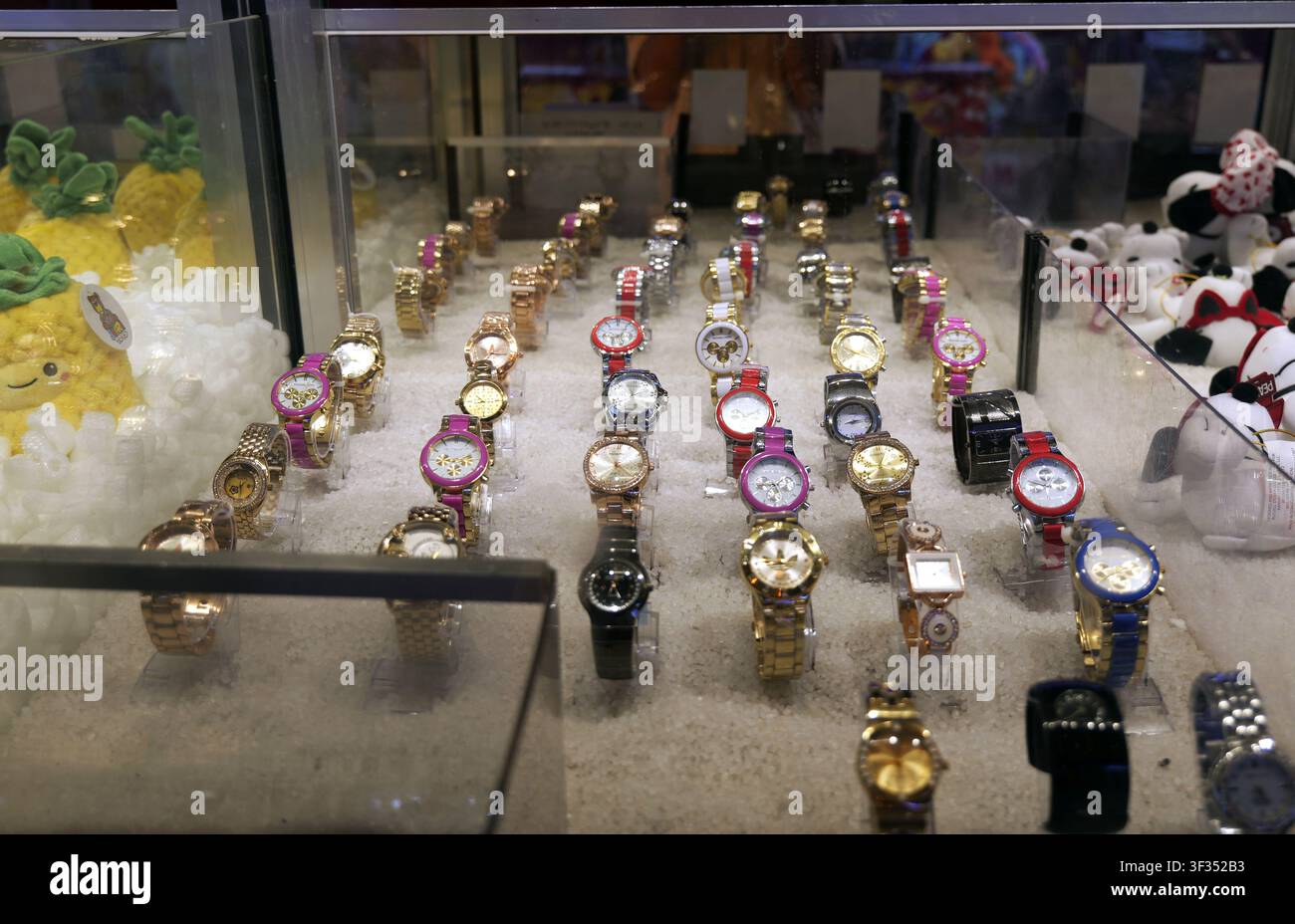 Montres-bracelets exposées dans une vitrine en verre d'un magasin, offrant divers designs et couleurs aux clients, avec des réflexions visibles sur le verre Banque D'Images