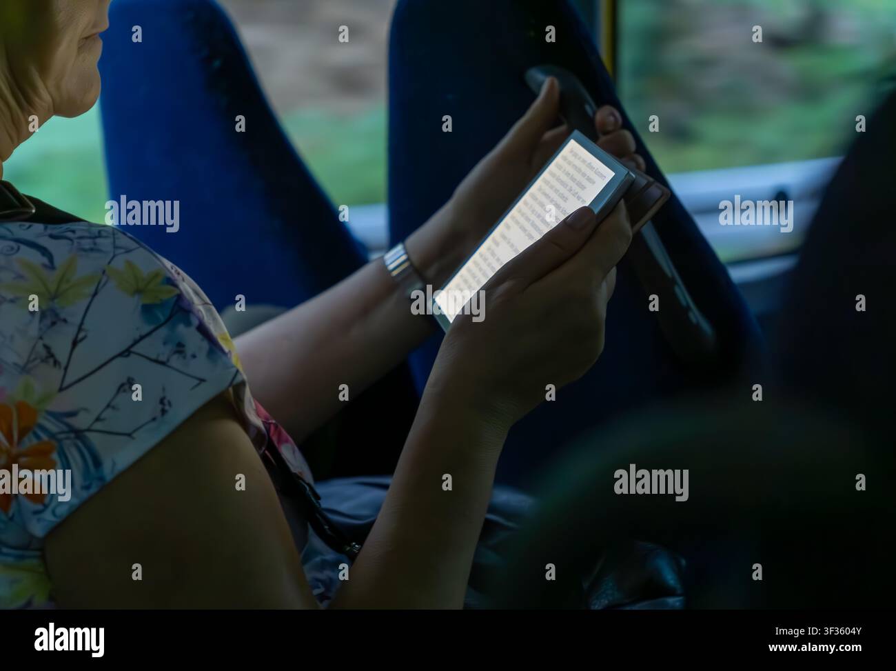 Grossissement d'une femme lisant un livre électronique sur une liseuse portable pendant qu'elle voyage dans un bus public. Passagère lisant un ebook, lecture numérique, mobile. Banque D'Images