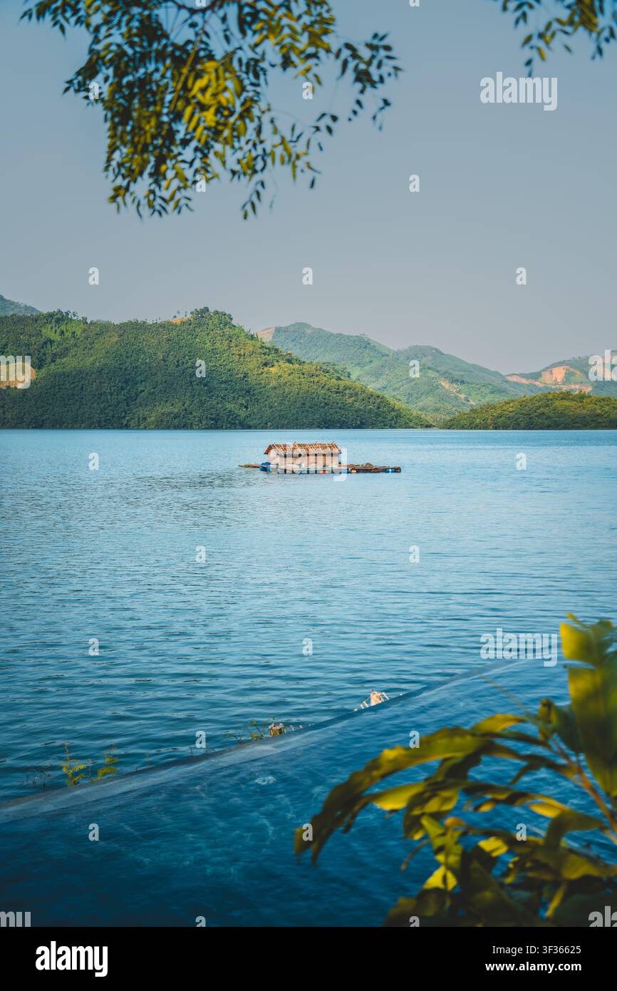 Maison sur radeau d'élevage de poissons flottante sur un lac bleu calme encadré par des feuilles et des montagnes vertes, Hoa Binh, Vietnam Banque D'Images