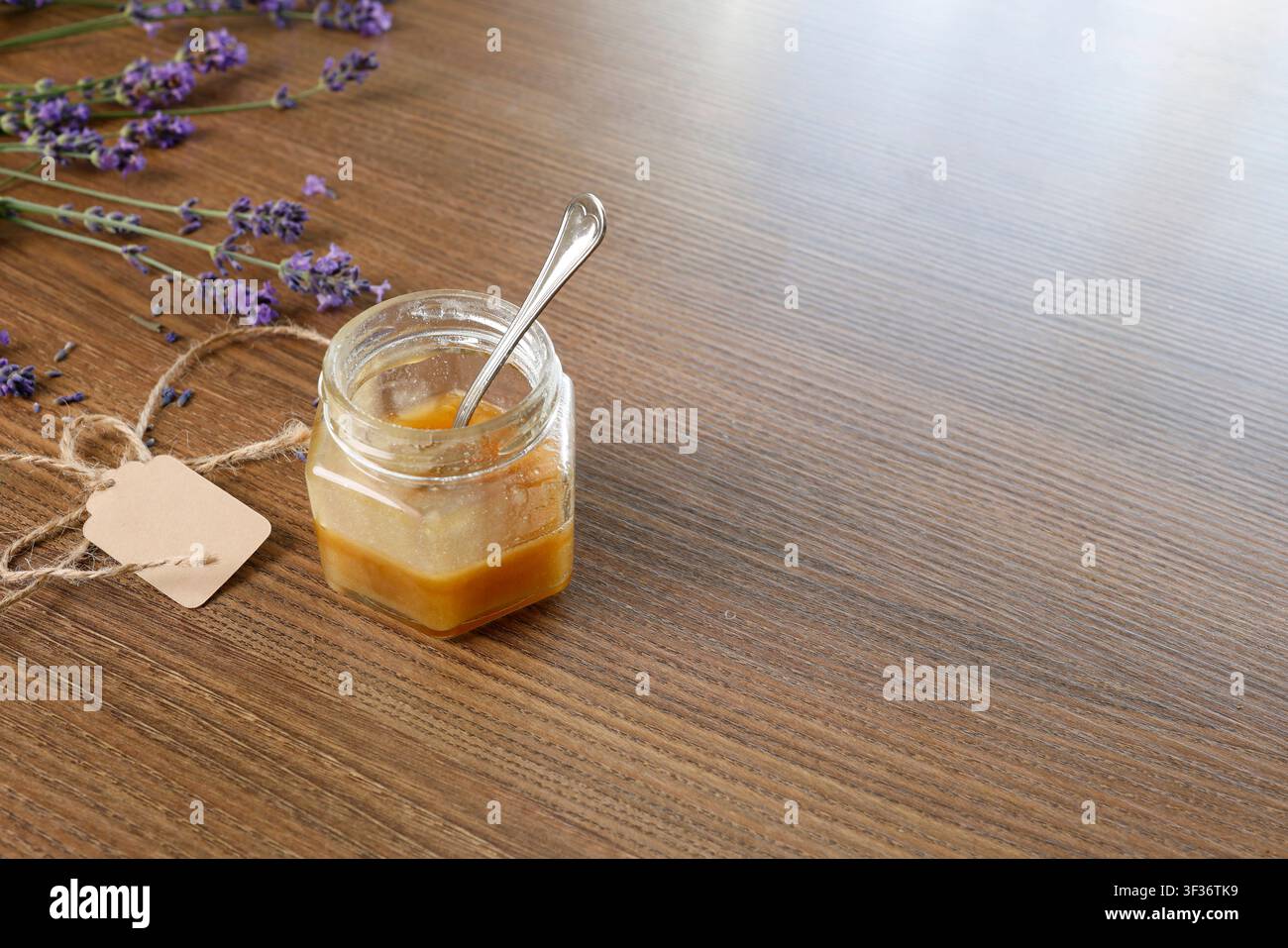 Vidéo d'un pot de miel sur fond lavande. Petit pot de miel ouvert avec une cuillère en argent et une étiquette kraft sur une table en bois. Concept de produit naturel biologique avec Banque D'Images
