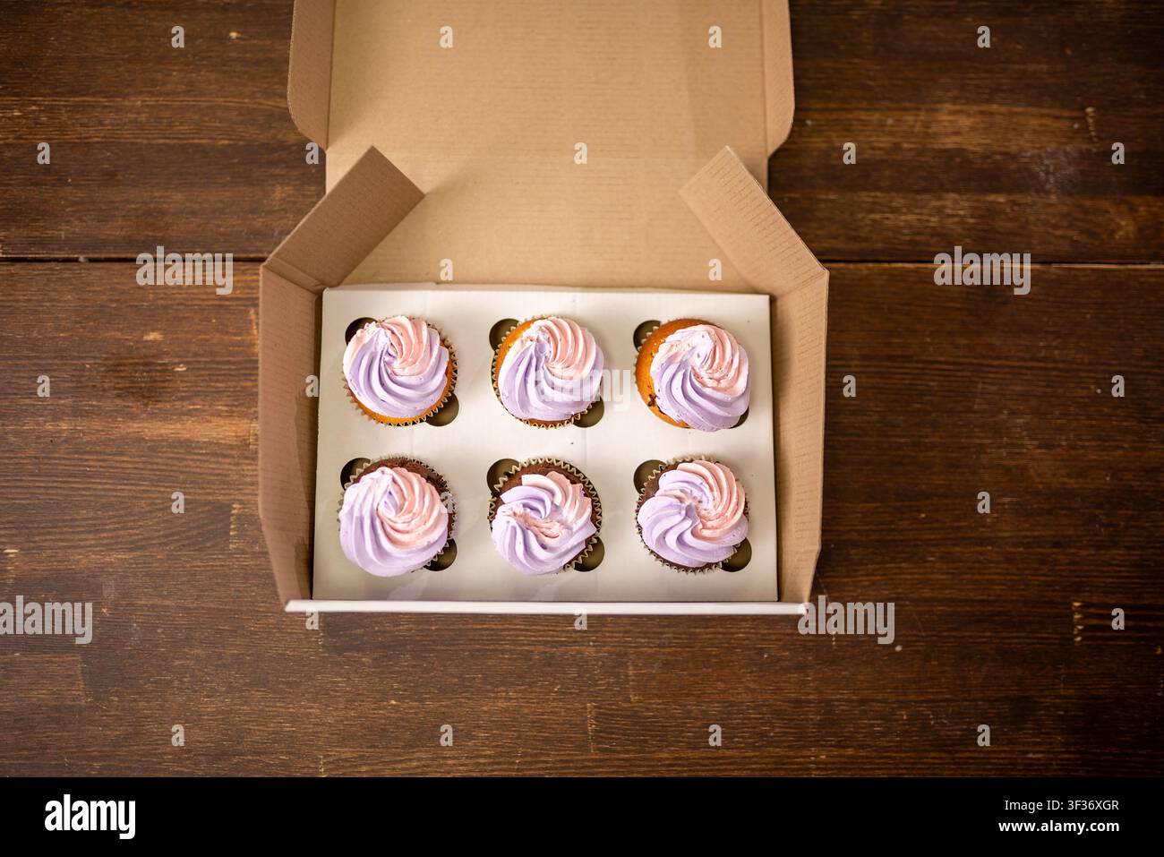 Boîte de six cupcakes givrés disposés dans une boîte de boulangerie en kraft sur une table en bois sous une lumière chaude Banque D'Images