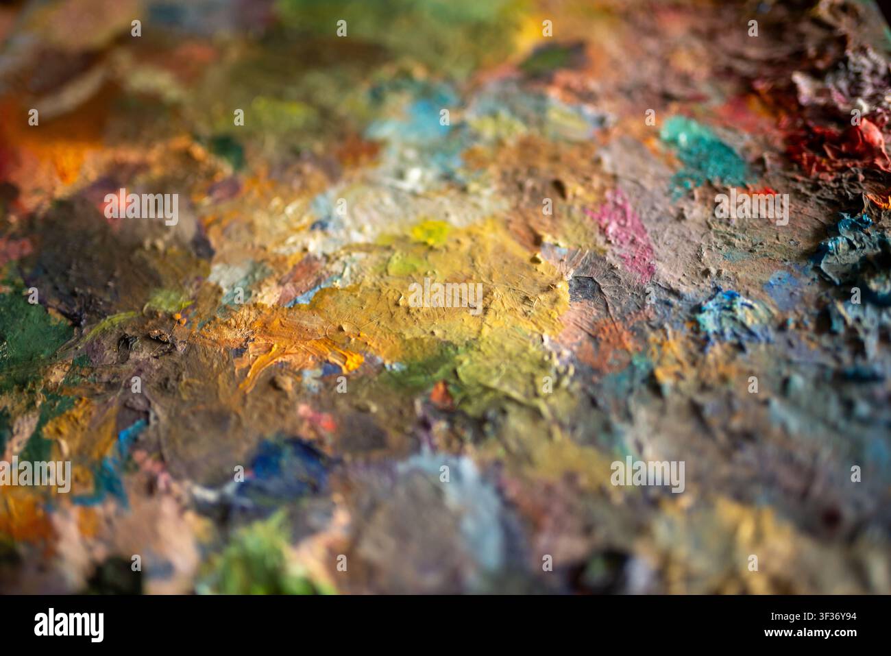 Gros plan de la surface de la palette du peintre avec des peintures à l'huile mélangées séchées et des coups de pinceau texturés dans des tons chauds Banque D'Images