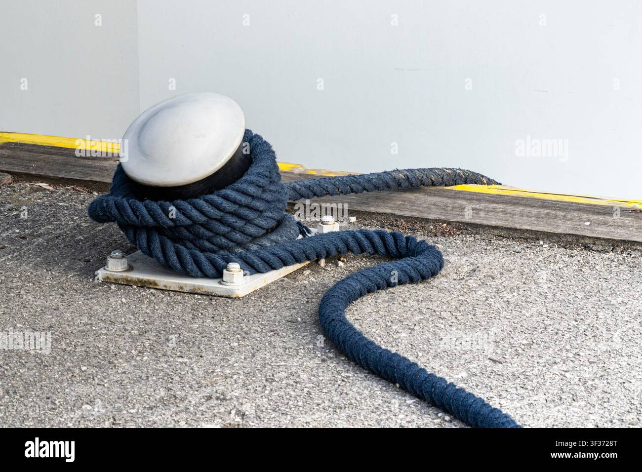Corde tressée bleue enroulée autour d'un bittement en métal dans une marina, illustrant le travail maritime et les responsabilités du quai. Banque D'Images