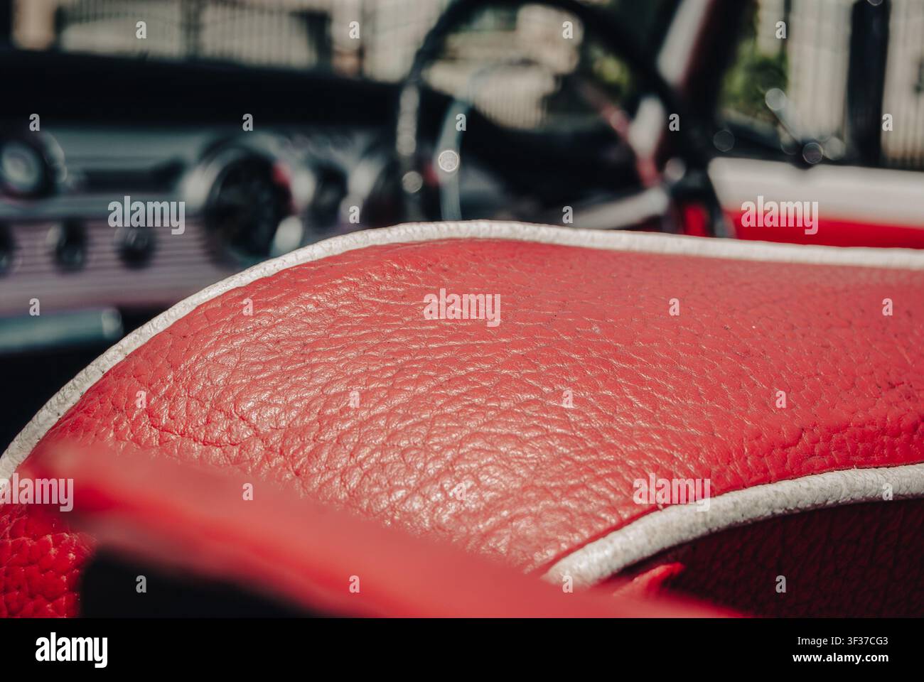 Grossissement macro d'un intérieur en cuir texturé rouge avec des passepoils blancs dans une voiture vintage classique, avec un tableau de bord flou en arrière-plan Banque D'Images