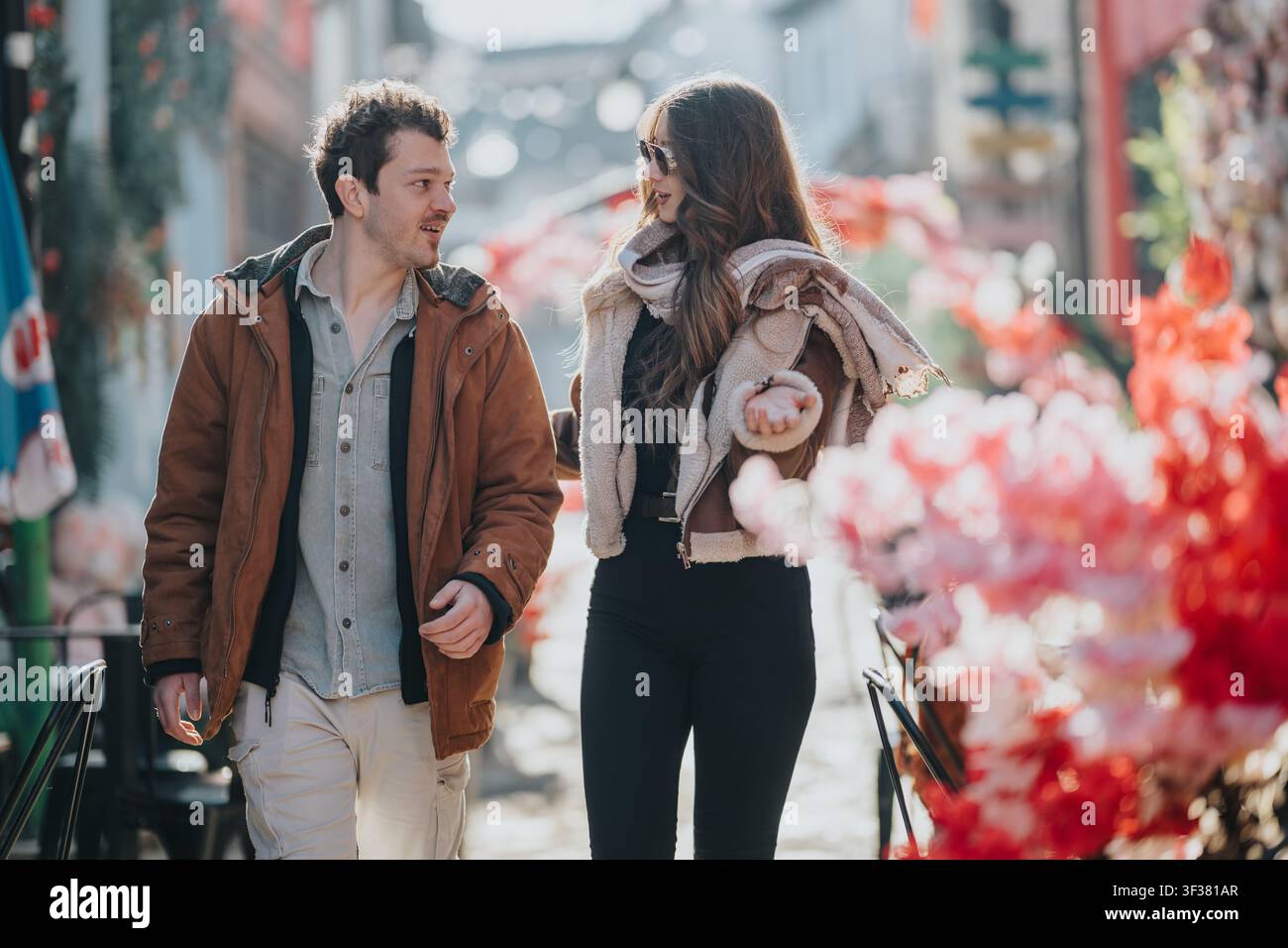 Jeunes amis marchant et discutant sur une rue de ville bordée de fleurs lors d'une sortie hivernale décontractée Banque D'Images