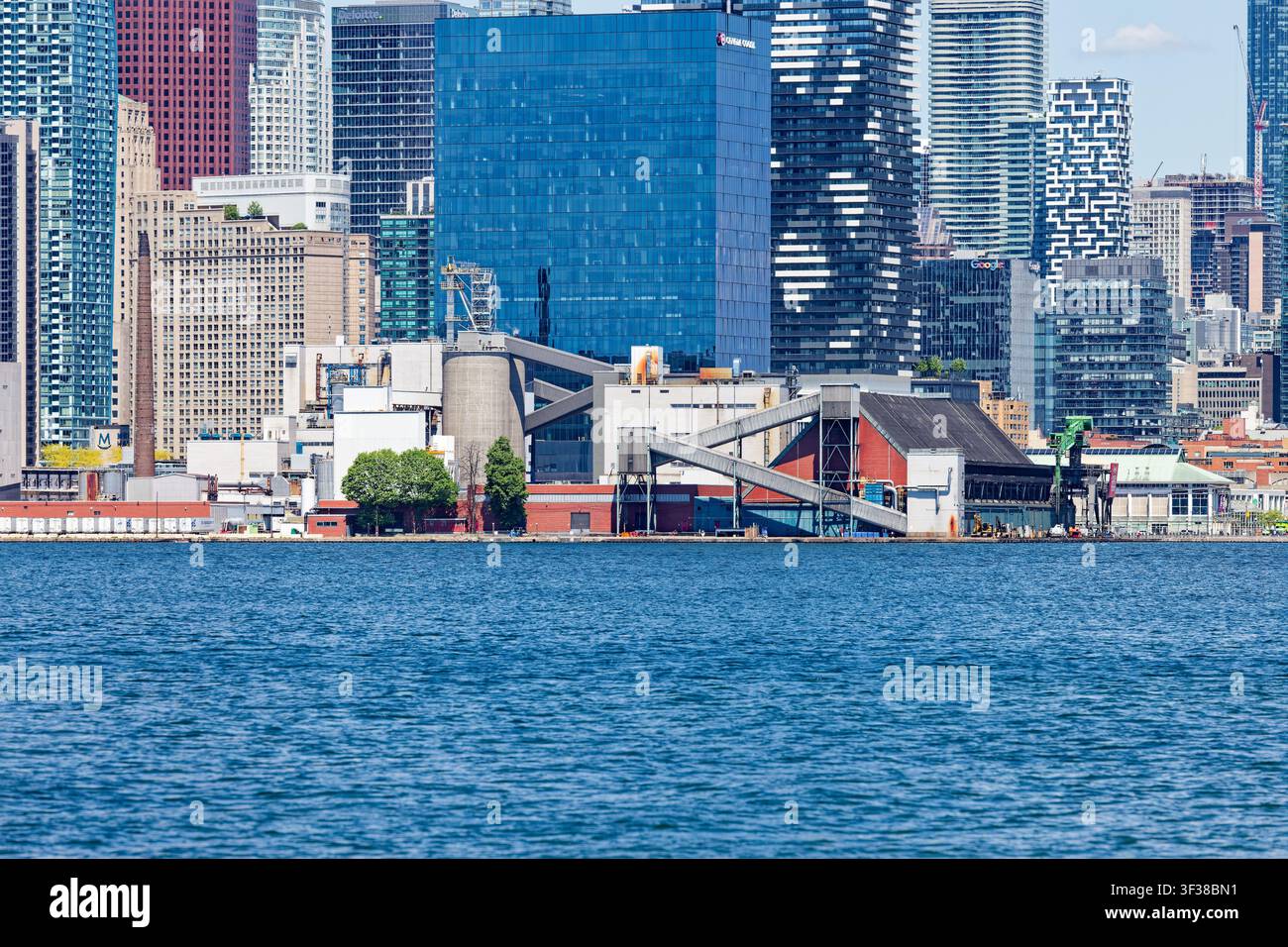 Une tour de bureau en verre bleu, 100 Queens Quay East, sert de toile de fond à l'usine Redpath Sugar, vue depuis Ward’s Island. Banque D'Images