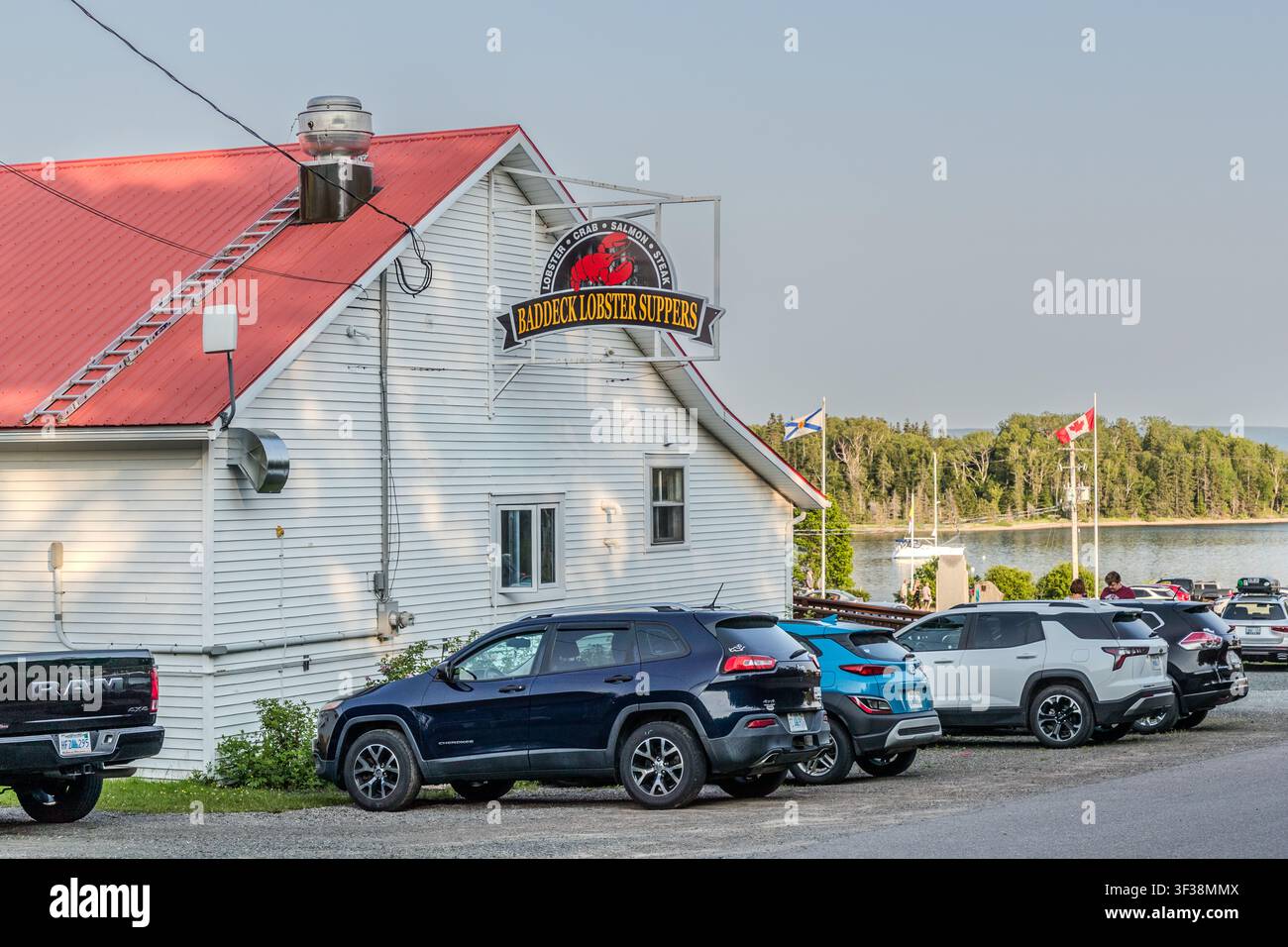 Le restaurant ‚Baddeck Lobster Suppers‘, avec son toit en tôle rouge et ses voitures garées, sur Ross Street à Baddeck, en Nouvelle-Écosse, Canada. La famille qui gère le restaurant peut regarder en arrière sur plus d'un siècle de tradition de pêche et sert du homard, du saumon cuit sur feu ouvert et d'autres spécialités locales dans un cadre de buffet Banque D'Images