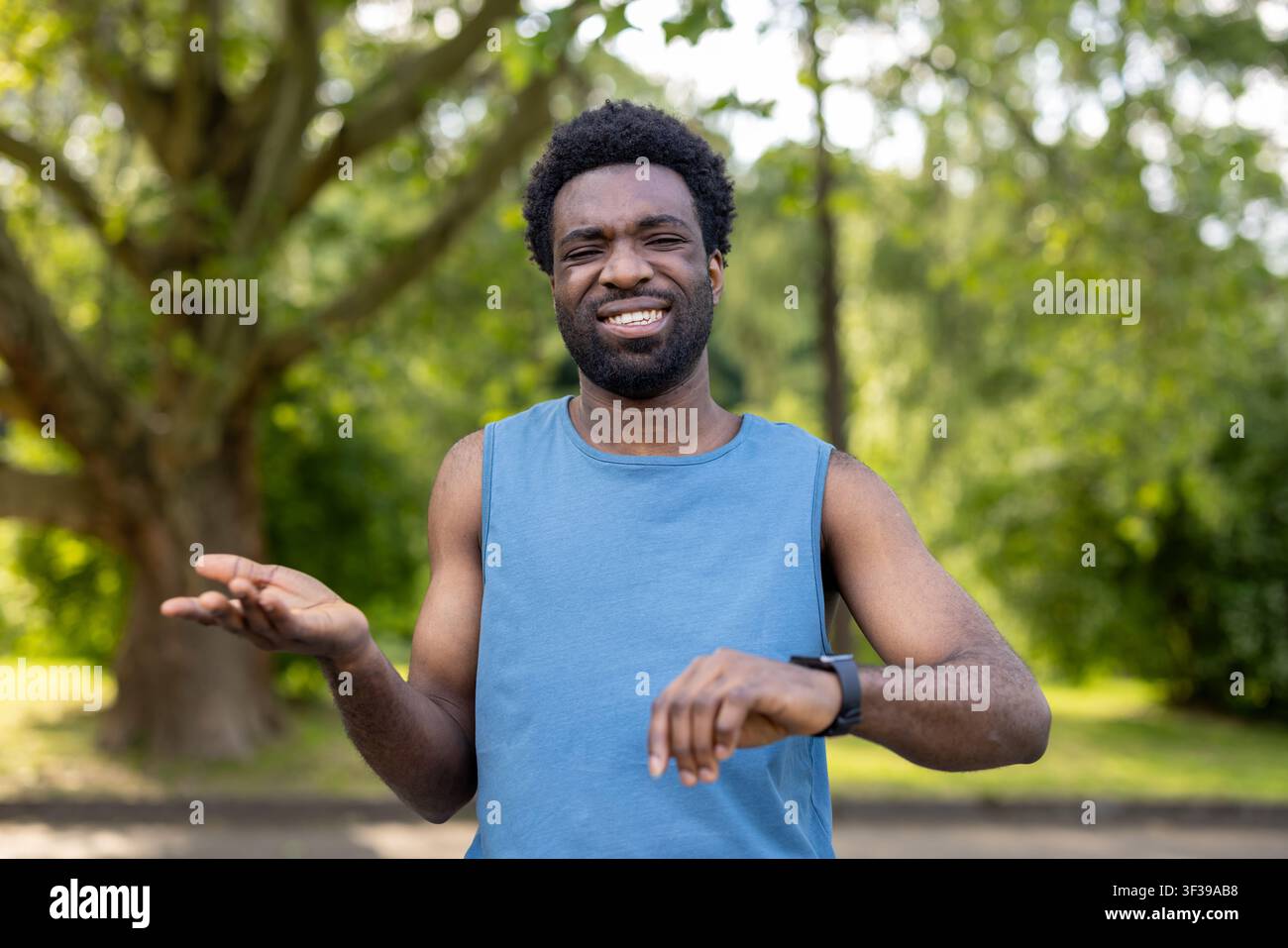 Jeune homme debout en plein air dans un parc, vérifiant sa montre intelligente avec une expression frustrée et exaspérée, indiquant des retards potentiels ou des objectifs d'entraînement manqués Banque D'Images