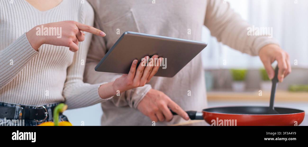 Couple cuisinant ensemble dans la cuisine, utilisant une tablette pour la recette, engagé et concentré Banque D'Images