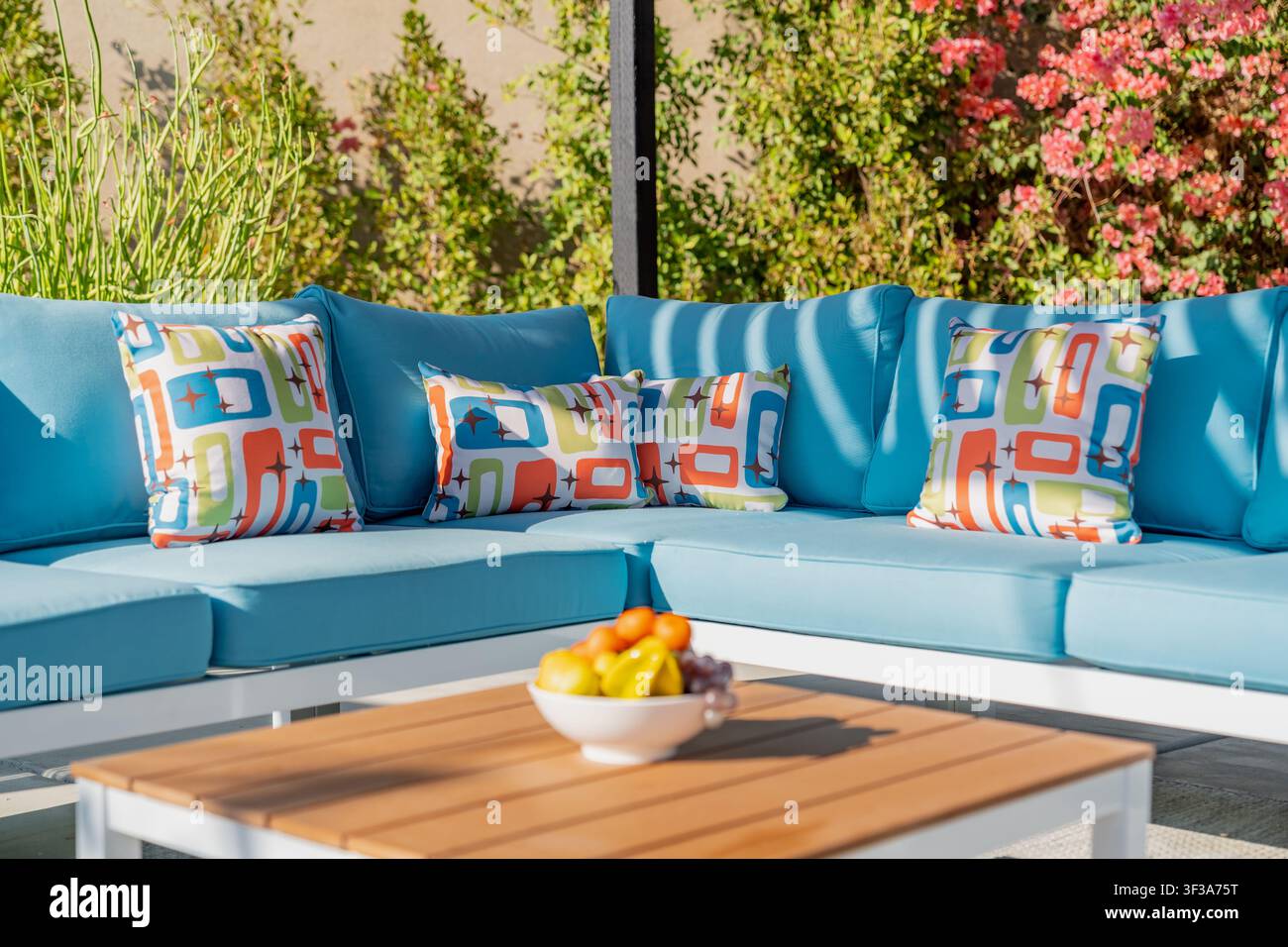 Un espace de détente extérieur vibrant met en valeur un canapé d'angle orné de coussins géométriques colorés et une table en bois portant un bol de fruits. Banque D'Images