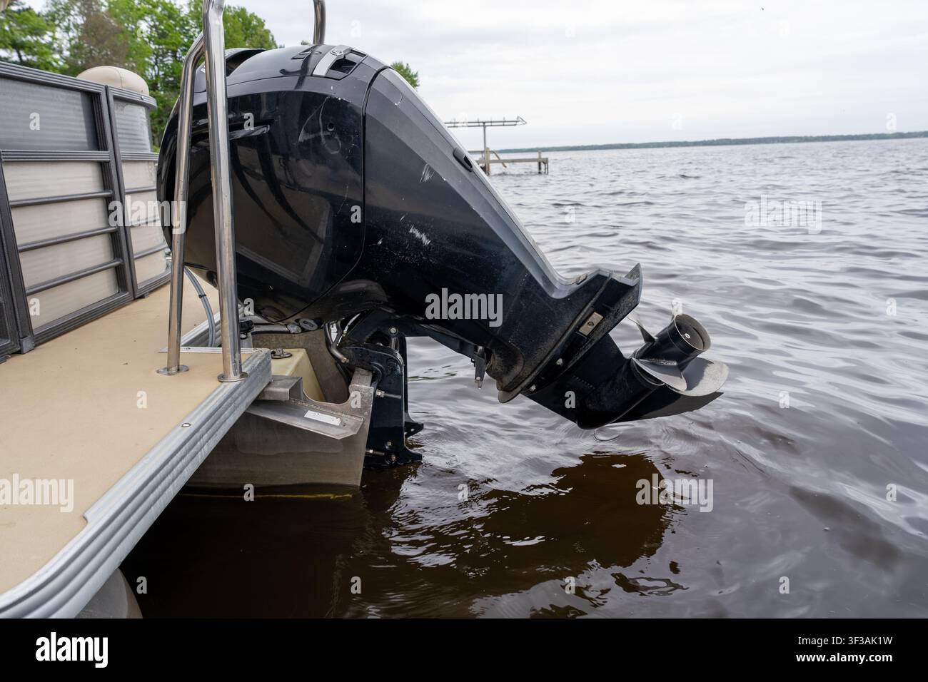 Une vue rapprochée en angle latéral d'un moteur hors-bord noir moderne installé à l'arrière d'un bateau à ponton flottant sur un lac serein. Banque D'Images